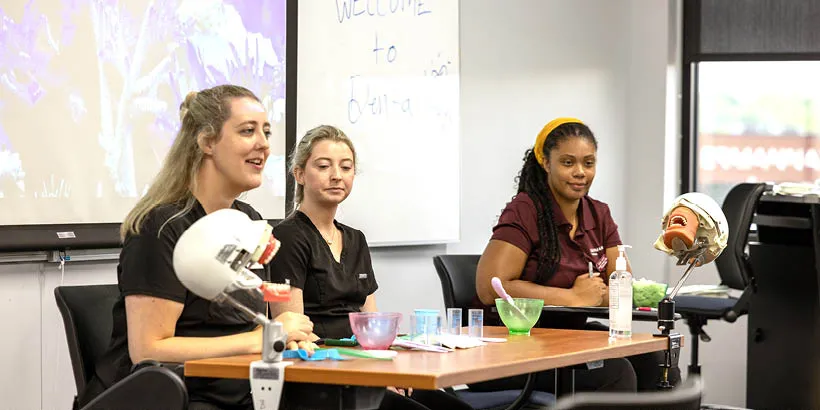 Three women demonstrate health science class models at an open house