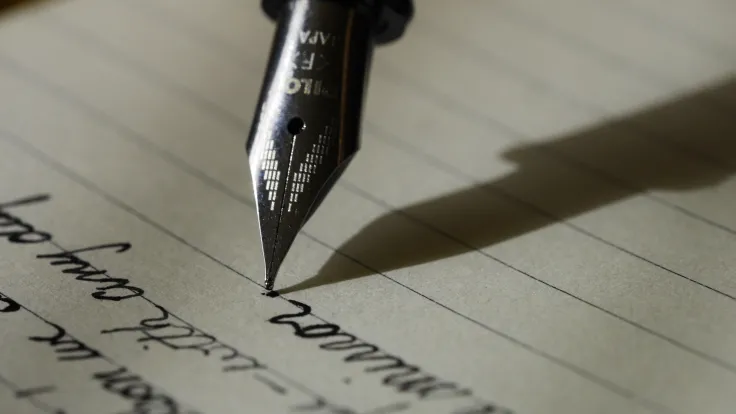 Calligraphy pen writing in cursive on paper courtesy of Aaron Burden from unsplash.com