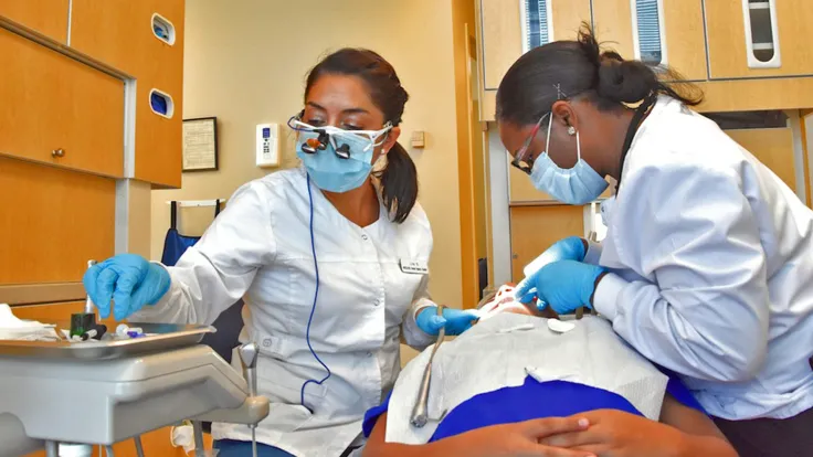 Two dental assisting technicians cleaning a persons teeth
