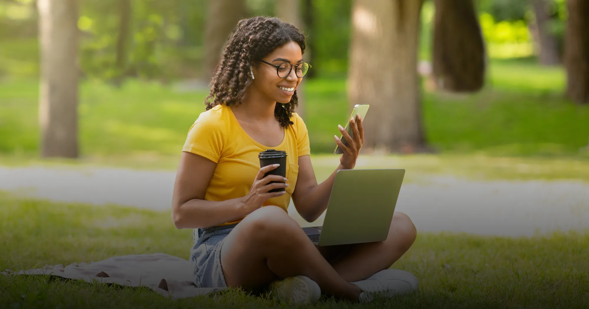 A woman relaxes outside on the grass while applying for summer classes on her phone
